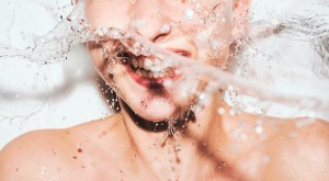 Eine junge, nackte Frau wird mit einer Flüssigkeit bespritzt - sie lacht; symbolisch für weibliche Ejakulation