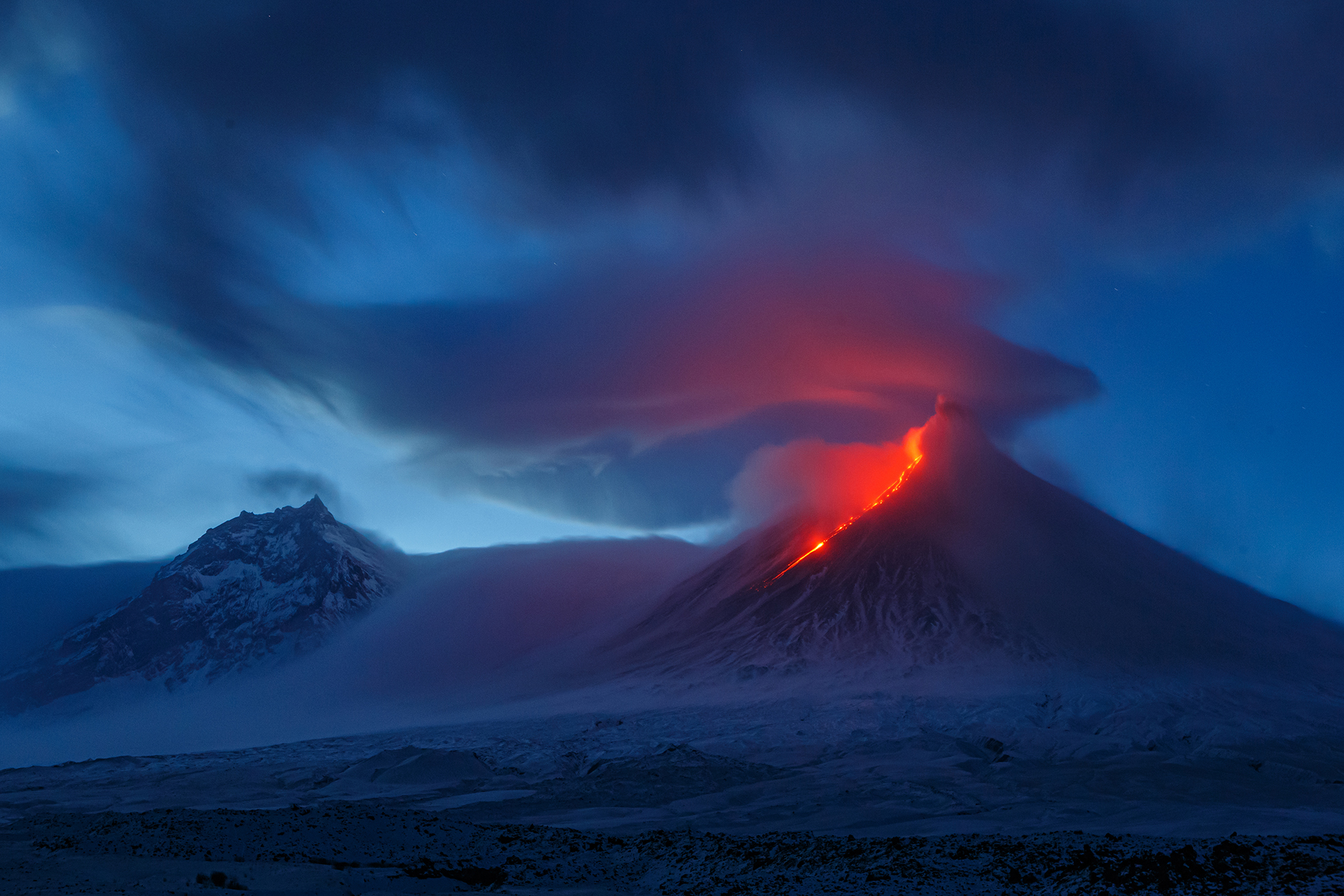 Die rot glühende Lava eines aktiven Vulkans beleuchtet die tief hängenden Wolken über dem Berg