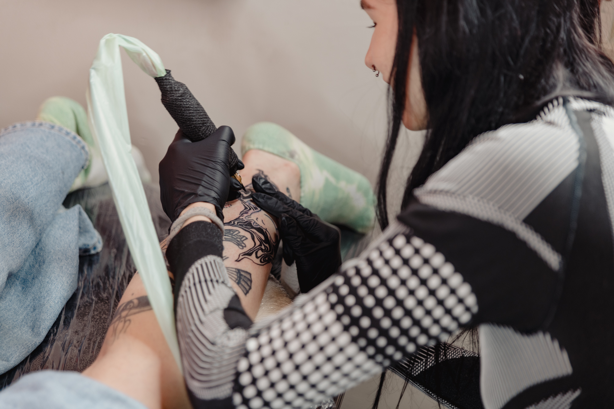 Polina Frank – young woman holding a tattoo needle, drawing on the back of someone's leg.